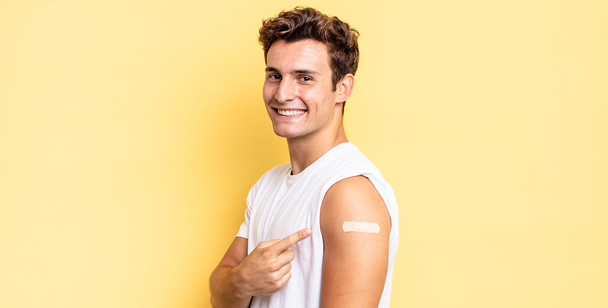 Young man smiling with a bandaid on his arm after receiving his vaccinearm with a bandaid after receiving her vaccine