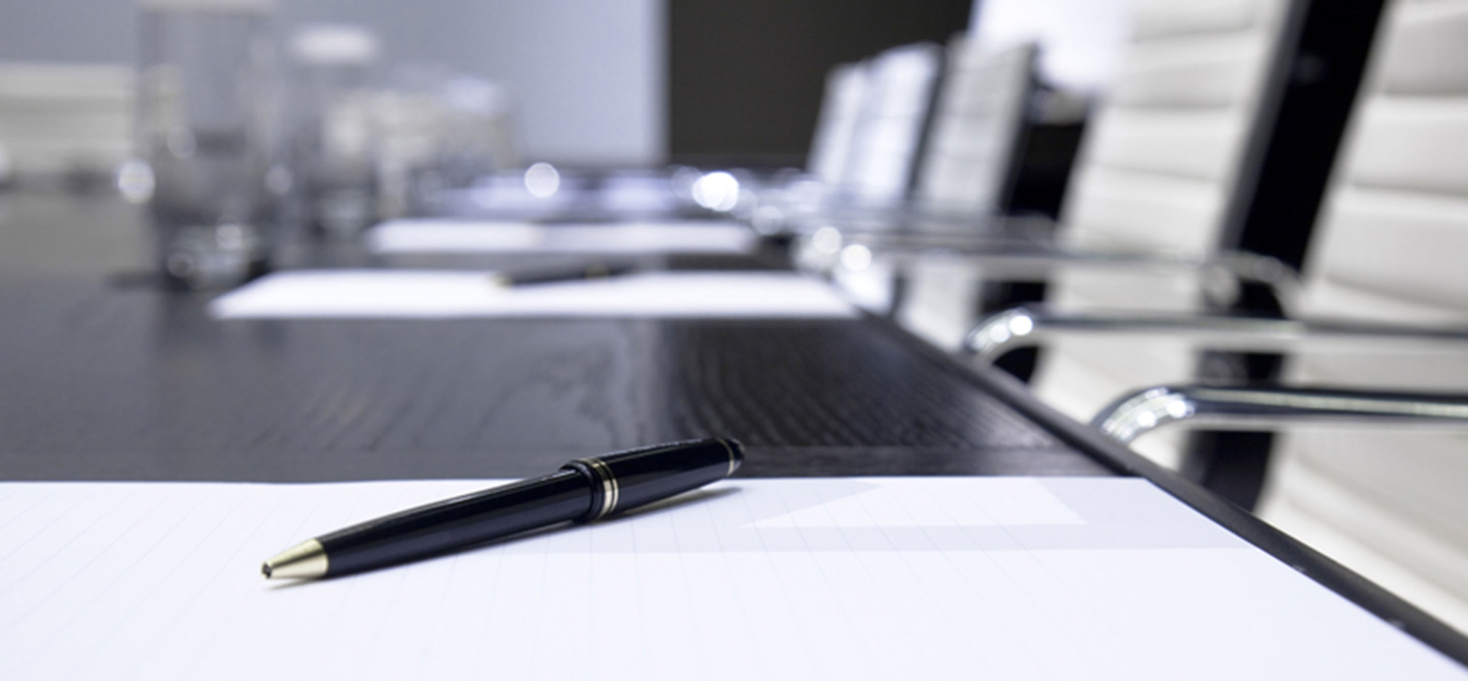 Corporate boardroom table set up for a conference with notepads and pens.