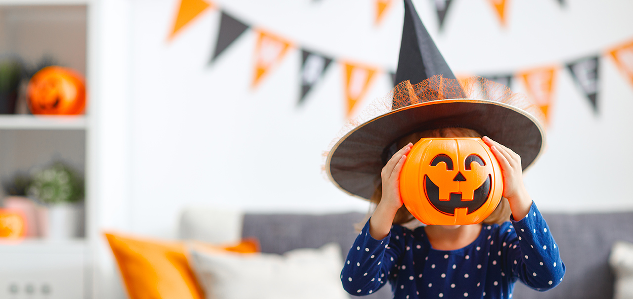 Little girl dressed as a witch holding up a smiling Halloween pumpkin trick-or-treat pail