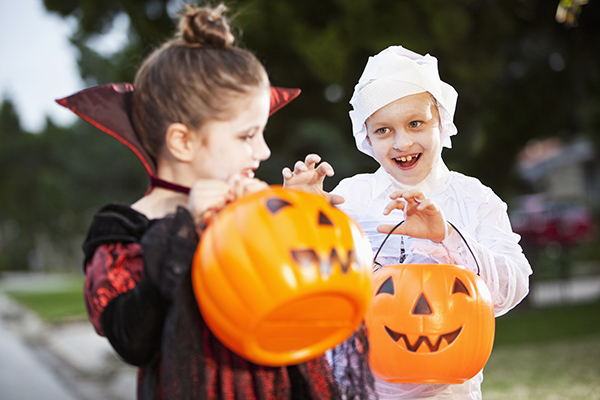 Halloween trick-or-treaters with pumpkin pails - Little boy dressed as a mummy playfully posing with little girl dressed as a vampire 