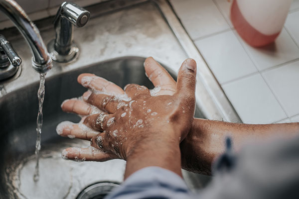 A man washing hands his hands with soap and water over a stainless steel sink