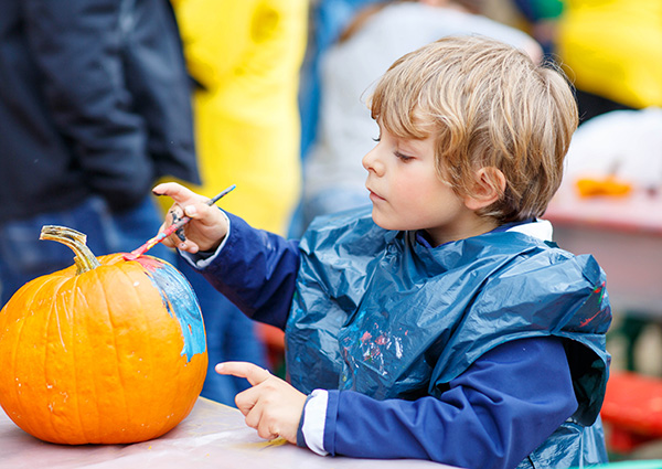 Young boy dressed in a smock painting a pumpkin at a Halloween fall festival party