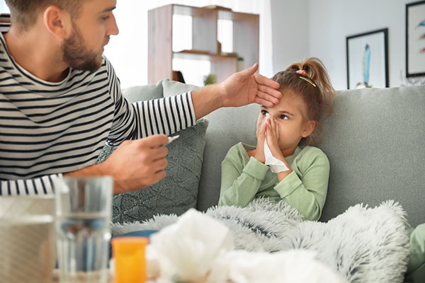 Child with a fever blowing nose with her father checking her forehead