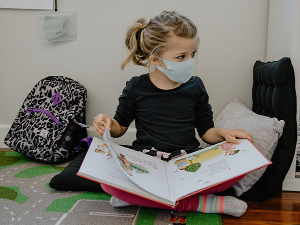 Young girl wearing a face mask over nose and mouth while reading a book at a school