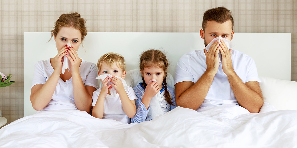 Family lying sick in bed with the flu, blowing their noses