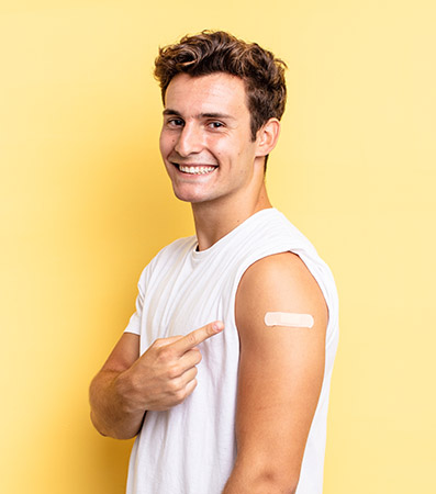 Smiling caucasian man with brown hair points at his arm where he received his COVID-19 vaccine