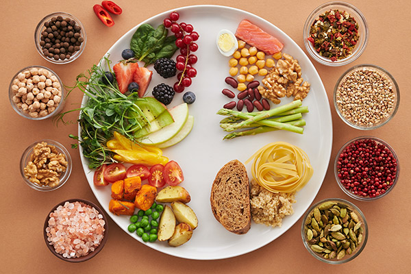 Seasonal produce on a plate featuring fresh fruits, raw vegetables, nuts, and seeds harvested in season