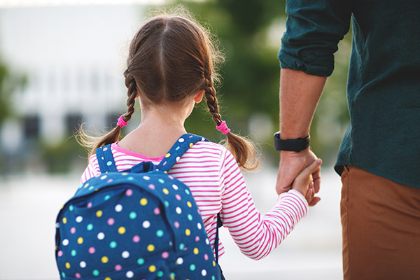 Young Student Wearing a Balanced Backpack with Both Straps Over Shoulders and Holding Parent's Hand