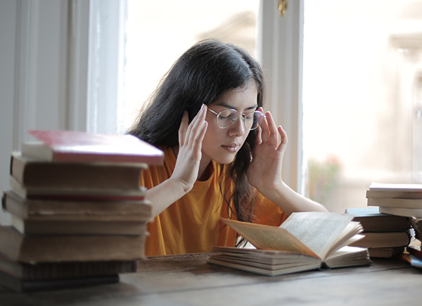 Tired Woman with Hands On Temples Suffering from Fatigue and Stress Leaning on a Table