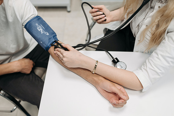 A man with a blood pressure cuff on his arm, having her blood pressure checked by a doctor / healthcare professional