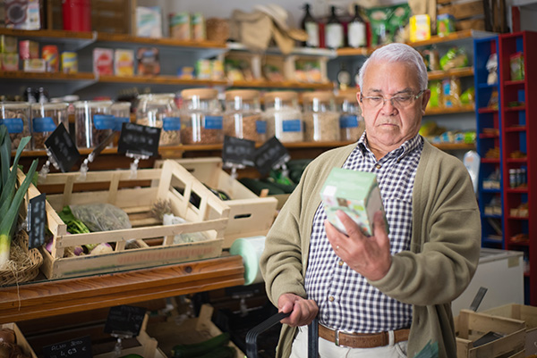 Senior Man in Checked Shirt with Glasses Reading Ingredient Label While Shopping at Grocery Store