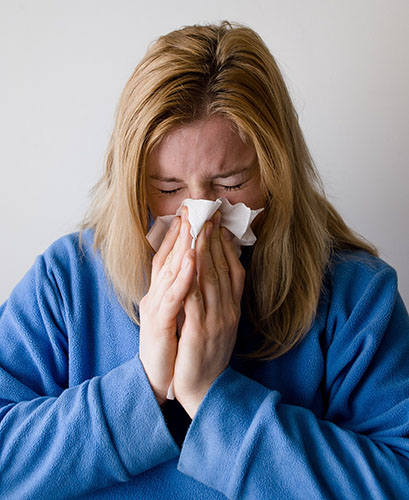 Sick blond woman in a blue sweatshirt blowing her nose