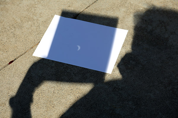 Photo of the solar eclipse safely projected onto a sidewalk using a pinhole projector fashioned from a sheet of paper