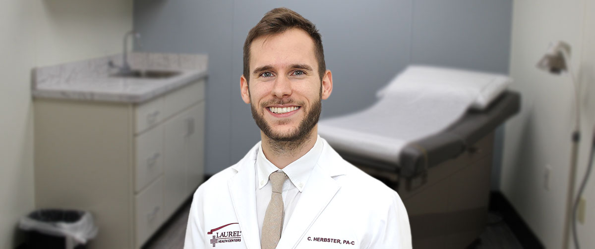 Christian Herbster, certified physician assistant (PA-C), standing in an exam room; Christian is seeing patients of all ages at the Elkland and Lawrenceville Laurel Health Centers.