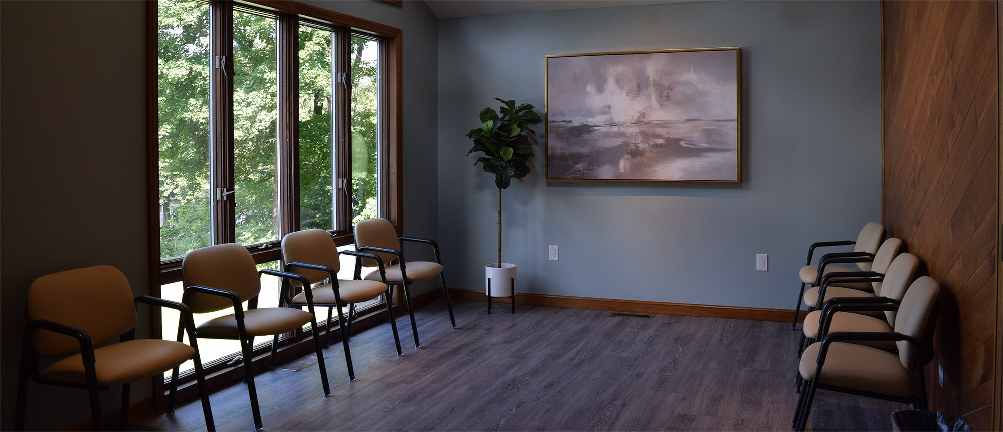 The waiting room for the Towanda Laurel Health Center. The room has two rows of chairs facing each other, an exterior window, a decorative plant, and a painting.